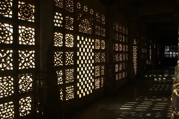 Sunlight falling through a pierced stone jali screen onto a dark floor